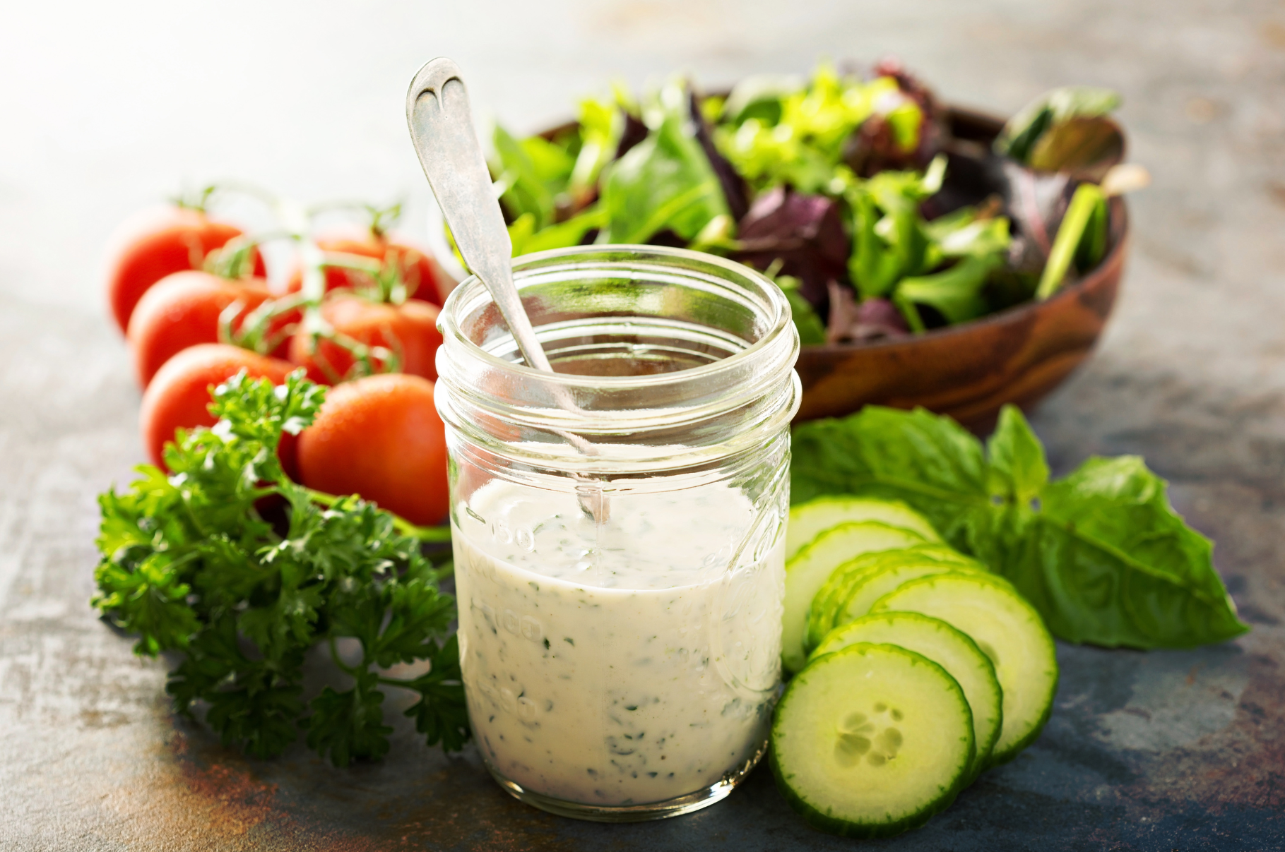 Image of Fresh homemade ranch dressing in a mason jar surrounded by cucumbers, tomatoes, herbs, and salad greens — Pro Chefly flavor made simple.