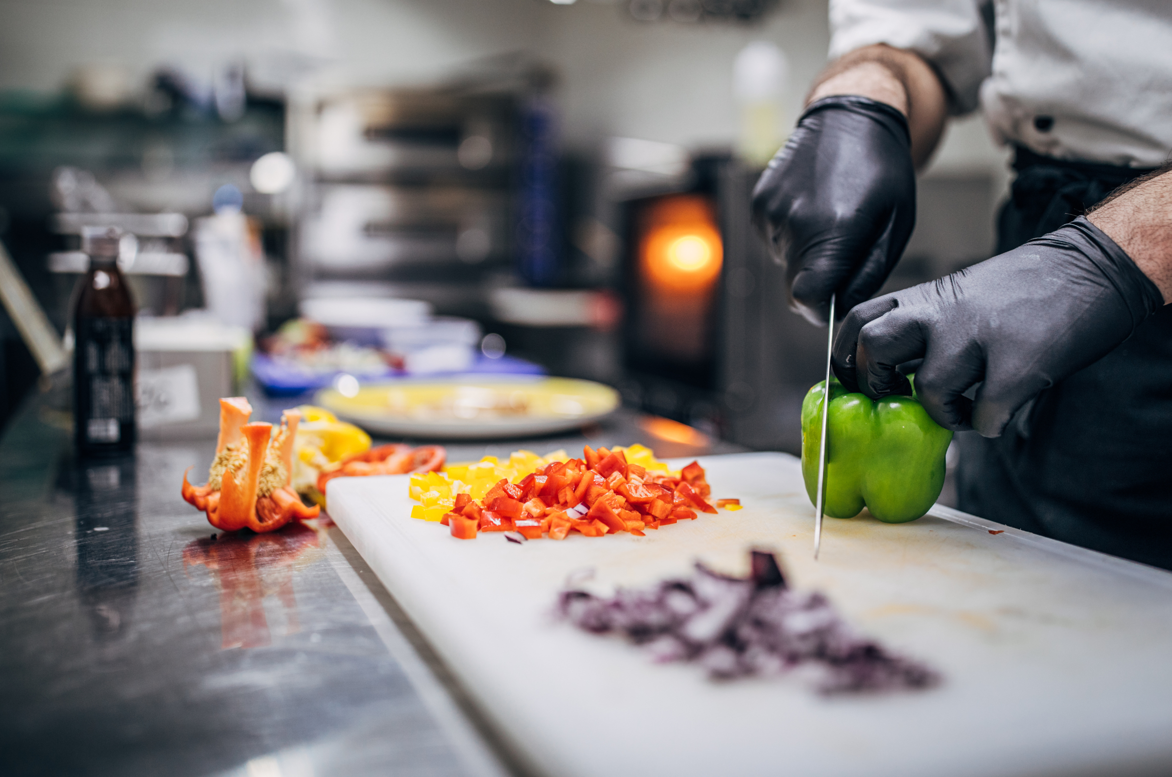 Image of Pro Chefly chef slicing bell peppers on a cutting board with diced onions and peppers nearby, showcasing precise prep work before using Japanese Damascus knives in the kitchen