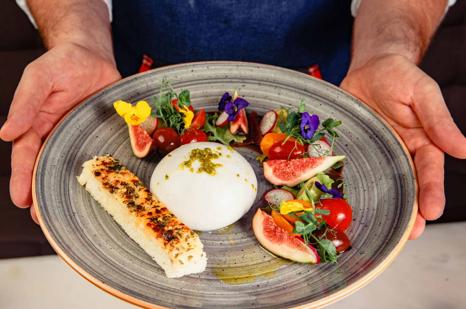 Chef presenting a colorful burrata plate with figs, tomatoes, and edible flowers—precisely prepped using a Pro Chefly petty knife for slicing and a paring knife for delicate garnishes.