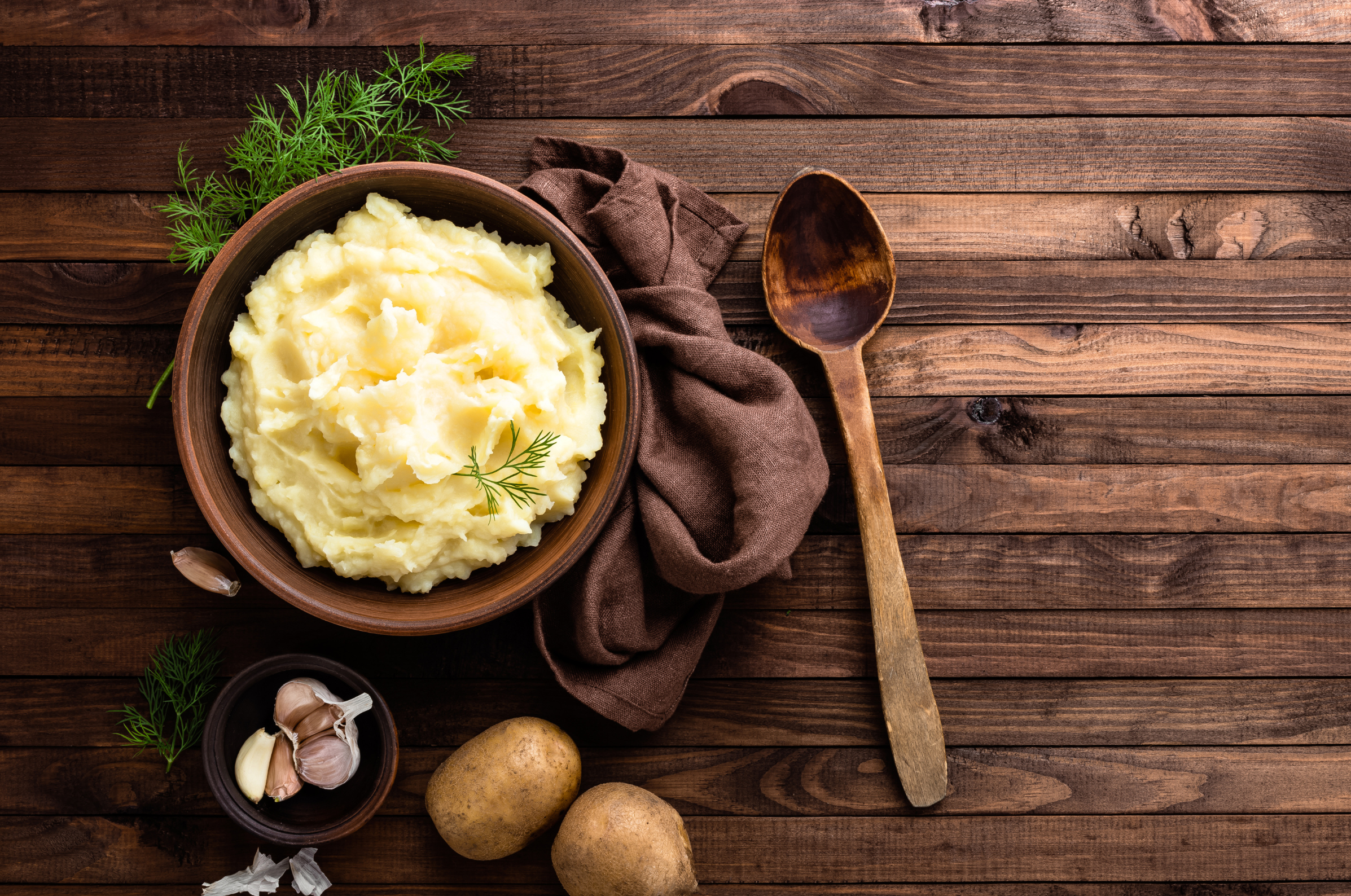 Image of Pro Chefly creamy mashed potatoes served in a rustic bowl on a wooden table with garlic and fresh herbs, ready for plating in a winter comfort dish
