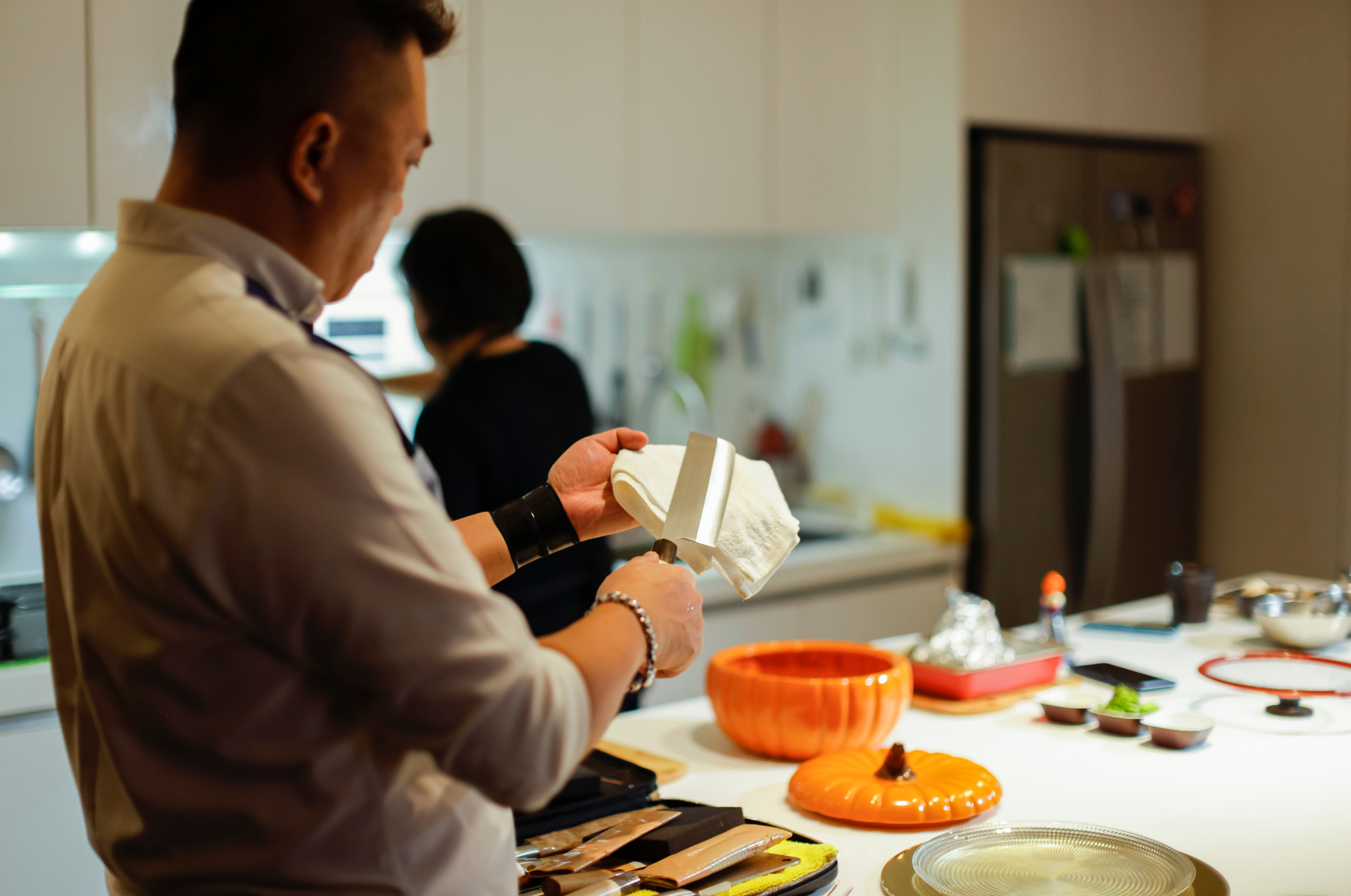 Pro Chefly chef carefully wiping down a Japanese knife with a cloth in a warm kitchen before prep, showcasing proper care and respect for premium blades