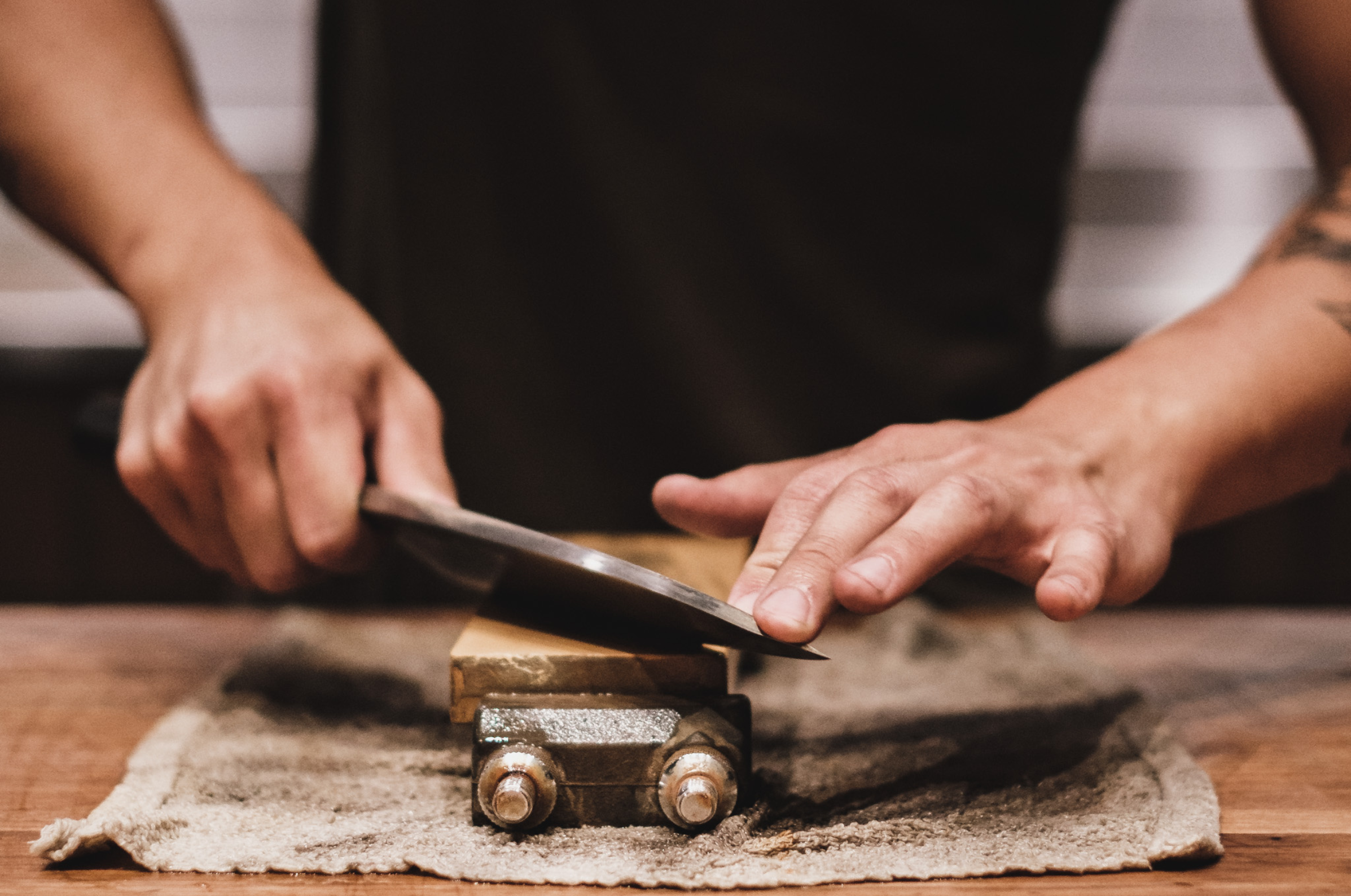 Pro Chefly Japanese knife being sharpened on a whetstone, captured close up to show angle, grip, and precise sharpening technique.
