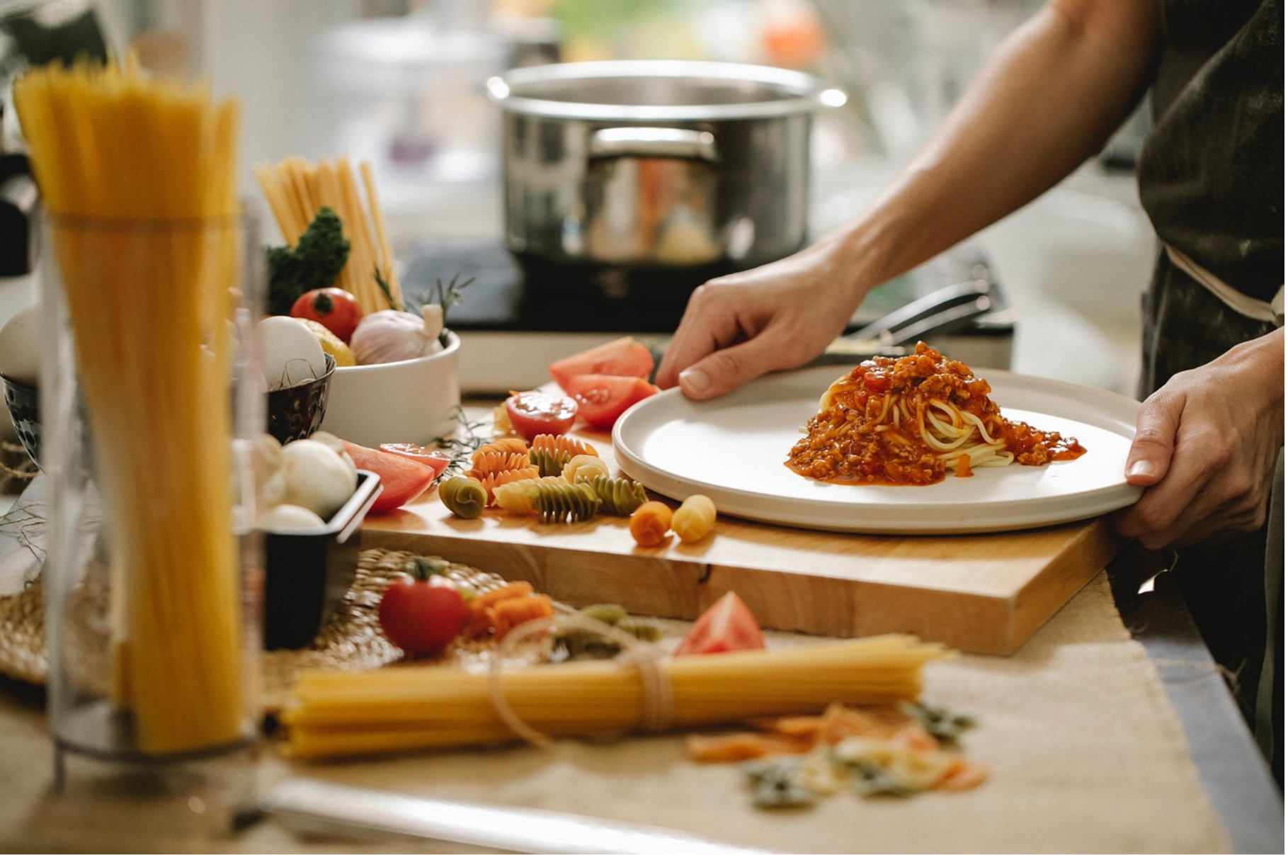 Chef plating fresh spaghetti with tomato sauce alongside uncooked pasta, tomatoes, and vegetables on a wooden cutting board – Pro Chefly kitchen scene