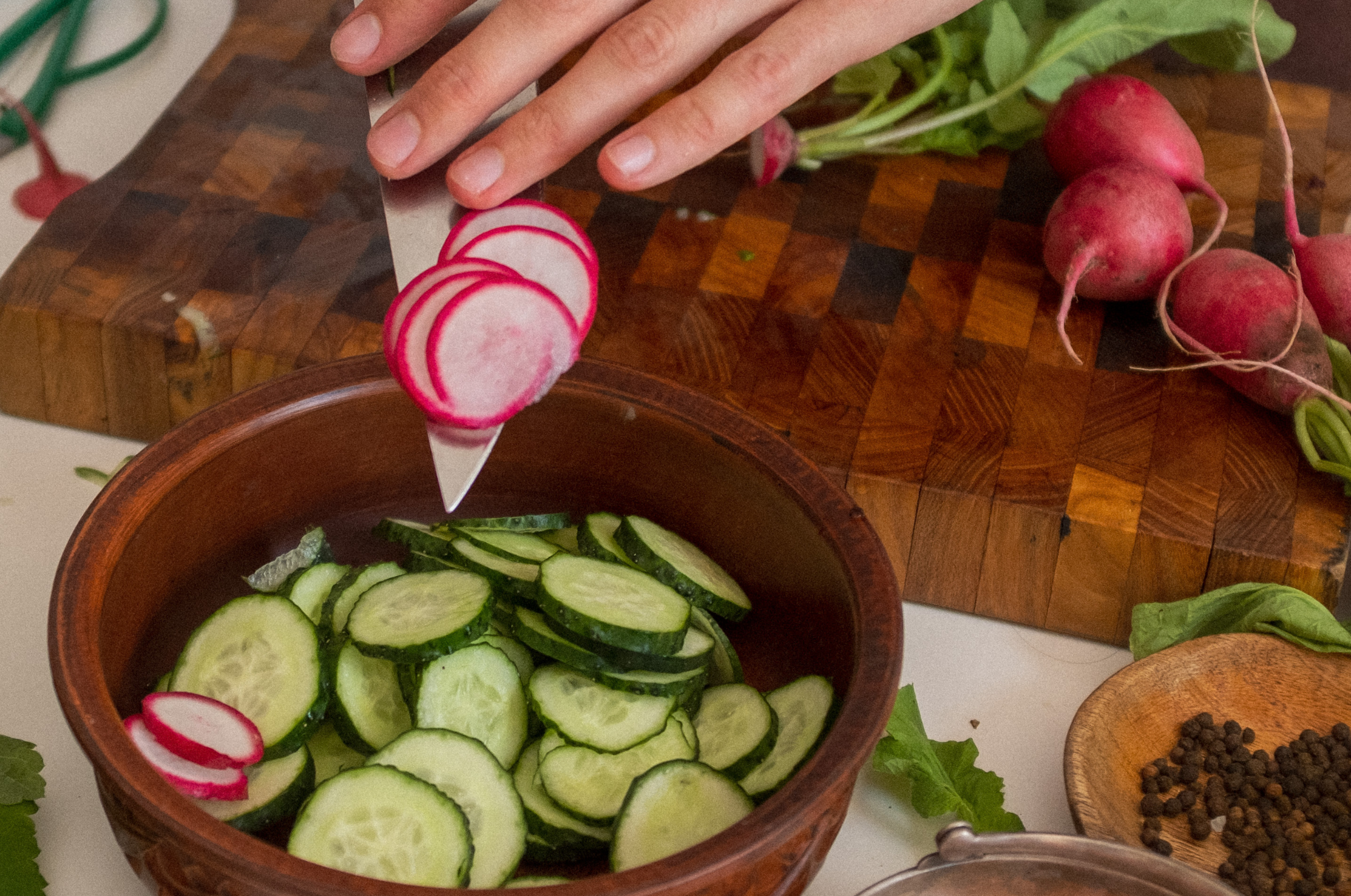 Pro Chefly Japanese knife slicing radishes over a bowl of cucumbers on a wooden board, showing precise cuts and fresh ingredients.