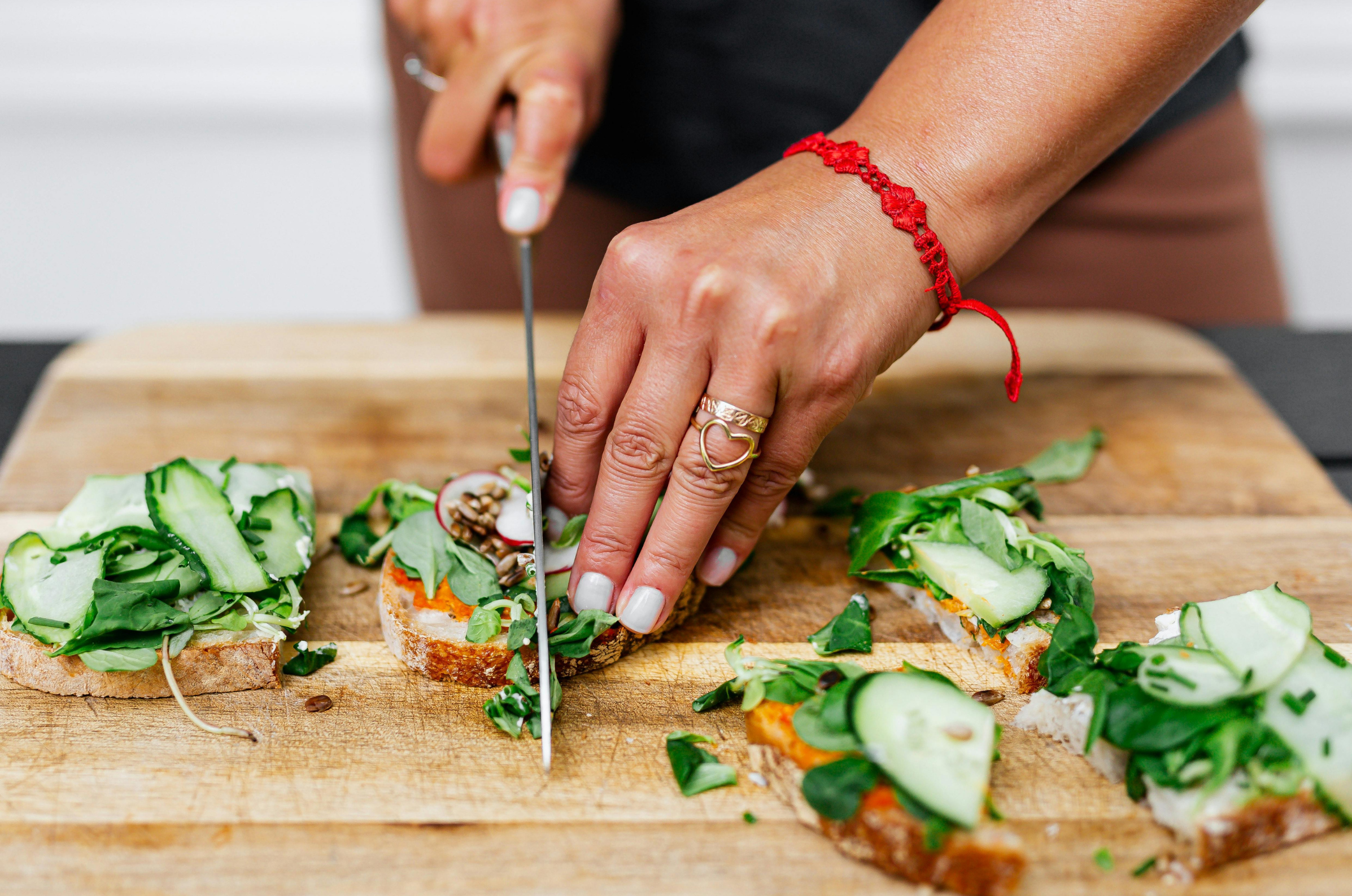 **Alt text:** Hands slicing vegetable-topped toast on a wooden cutting board.