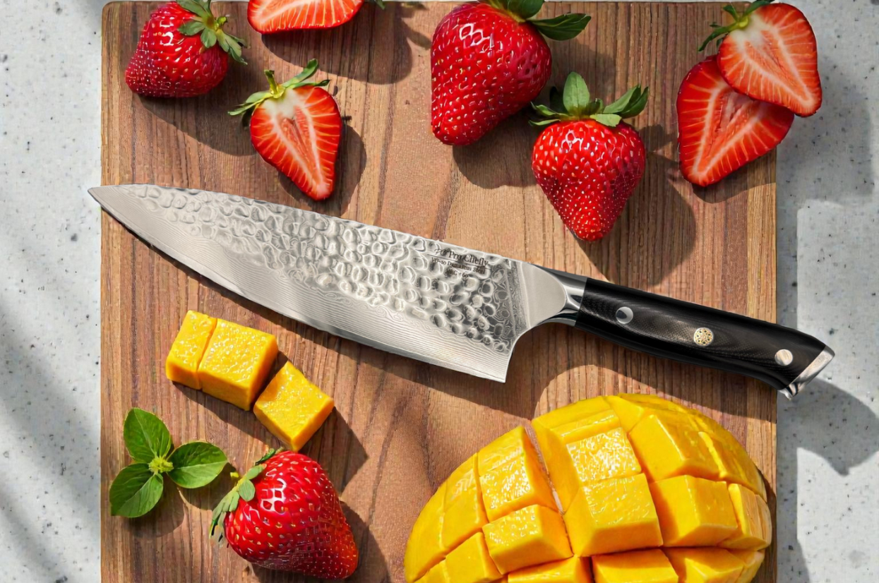 **Alt text:** Damascus chef knife on a wooden board with sliced strawberries and cubed mango.