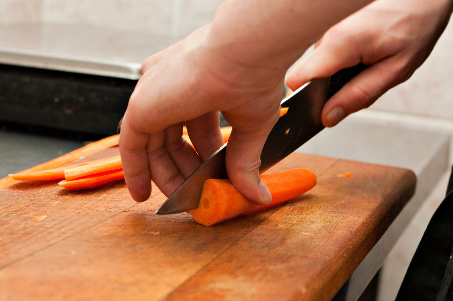 Chef slicing fresh carrots on a wooden cutting board using a sharp Pro Chefly Damascus Japanese knife for precise, clean cuts.