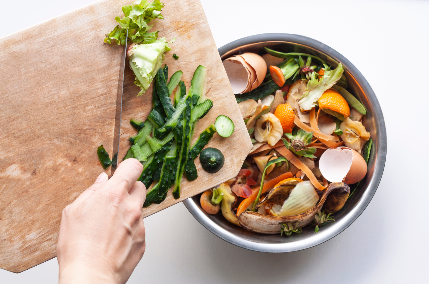 Image of Chef using a Pro Chefly Damascus Santoku knife to slice cucumbers and vegetables on a wooden board, with fresh produce scraps collected in a stainless steel bowl beside it.