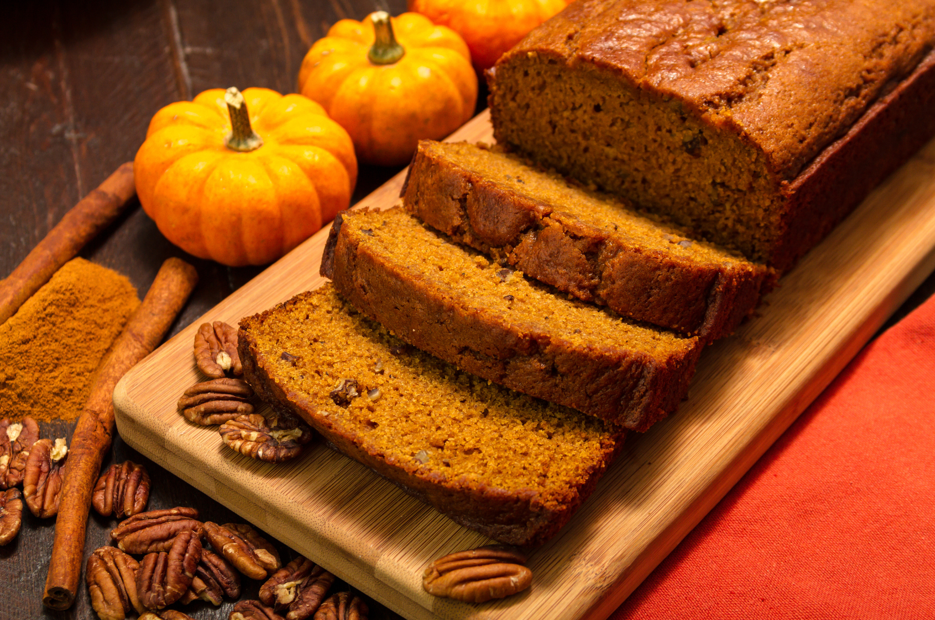 Freshly sliced pumpkin bread on a wooden cutting board surrounded by mini pumpkins, pecans, and cinnamon sticks, perfectly cut with a Pro Chefly Damascus bread knife.
