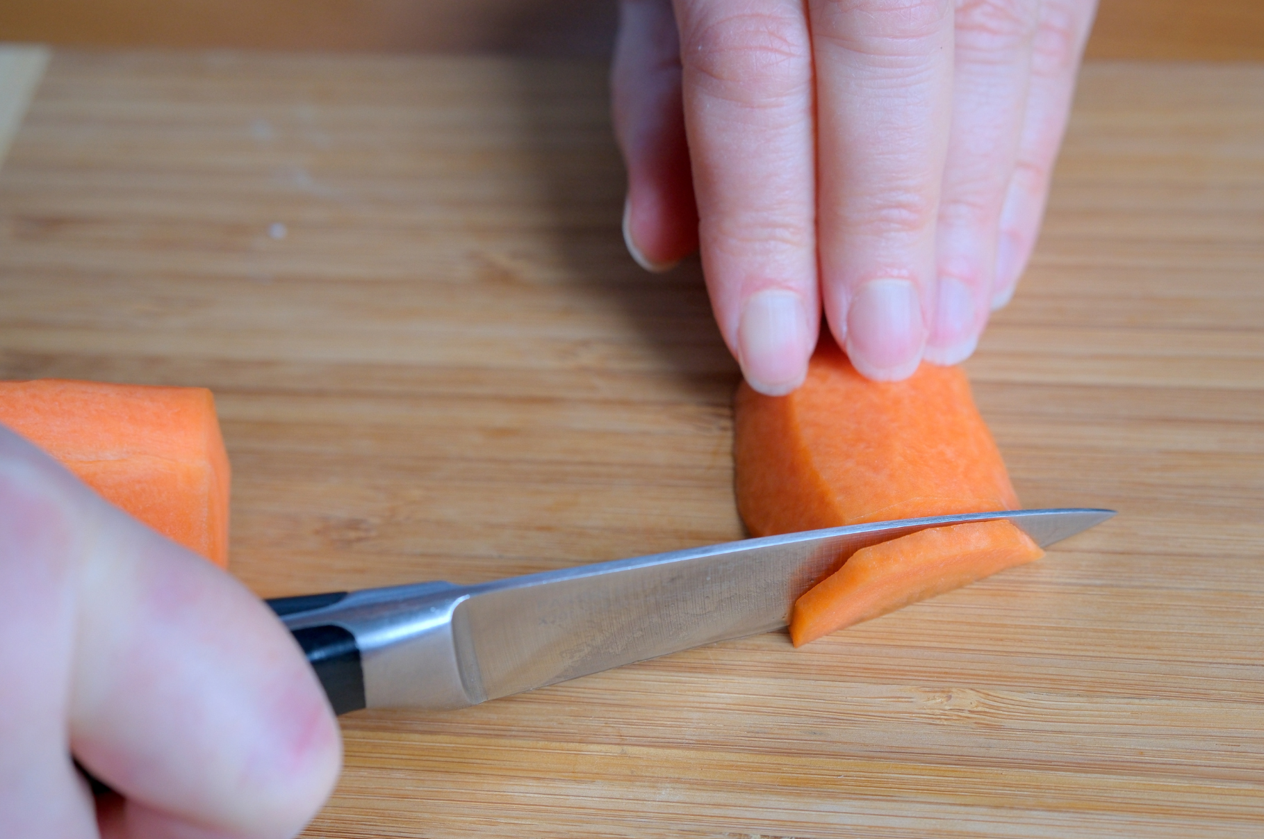 Chef slicing a carrot with precision using a Pro Chefly Damascus paring knife on a wooden cutting board for fine vegetable prep.