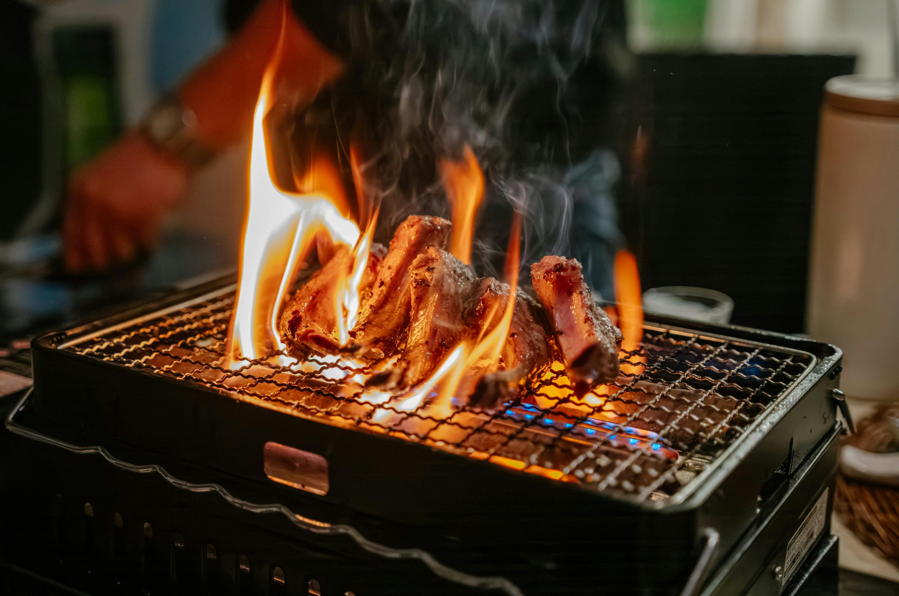 Flames rise around sizzling ribs on a hot grill — a bold display of fire, flavor, and craftsmanship that captures the passion behind Pro Chefly’s cooking experience.