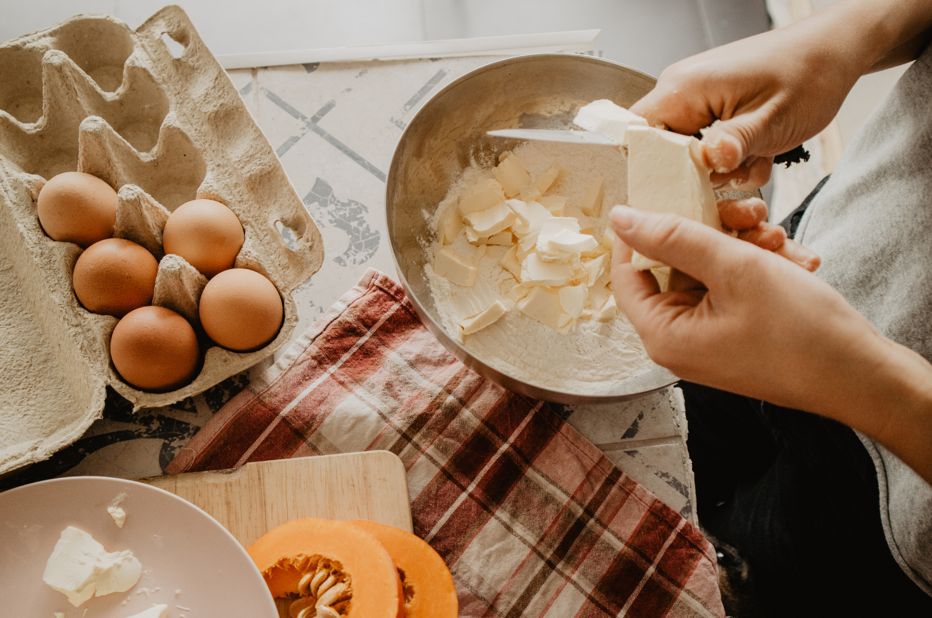 Image of Home baker slicing butter into a bowl of flour beside fresh eggs and pumpkin — a cozy kitchen scene that reflects Pro Chefly’s dedication to precise tools and seasonal cooking.
