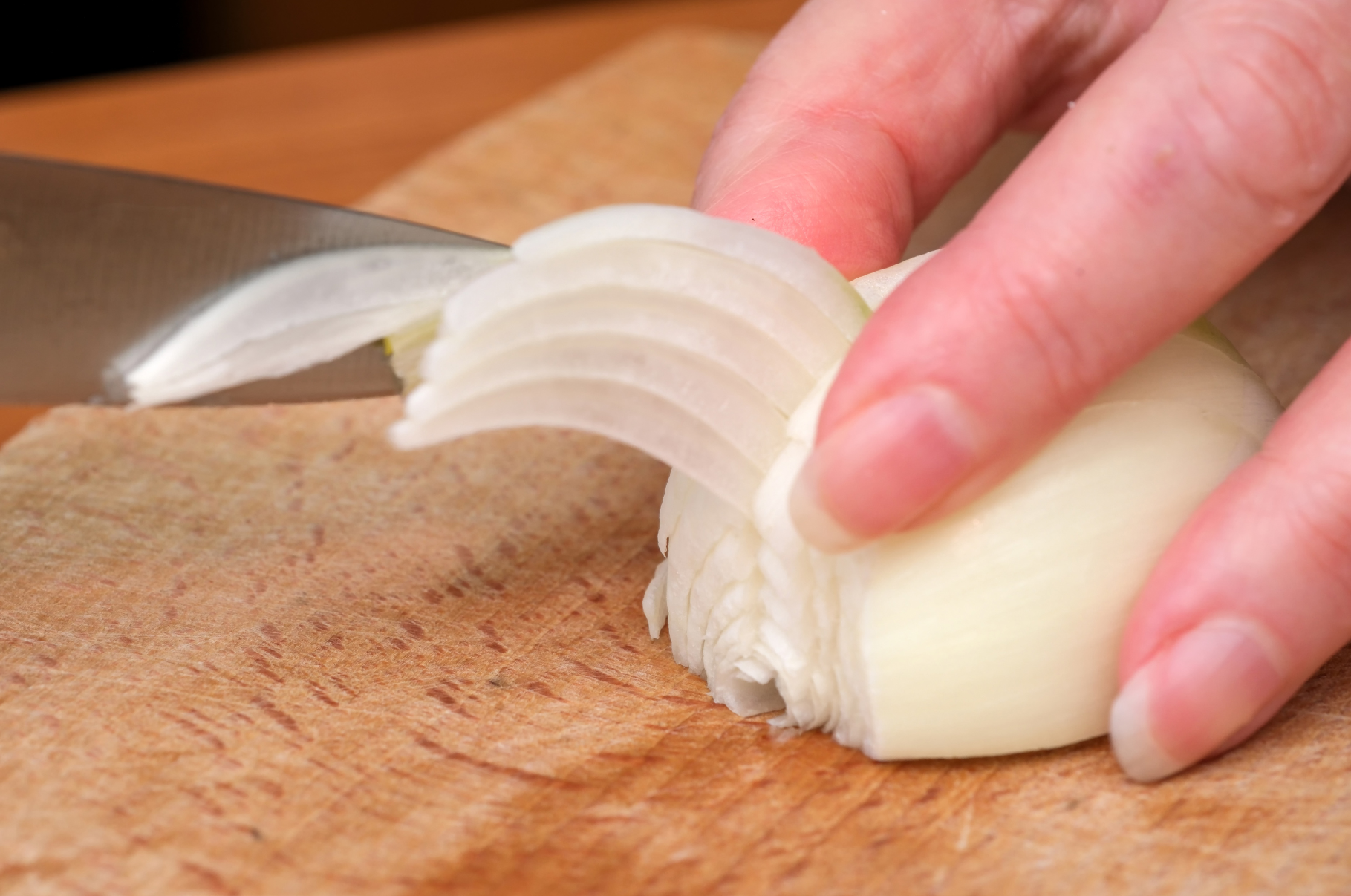 Close-up of a Damascus knife finely slicing a white onion on a wooden cutting board — showcasing the sharp precision and control of Pro Chefly’s handcrafted blades.