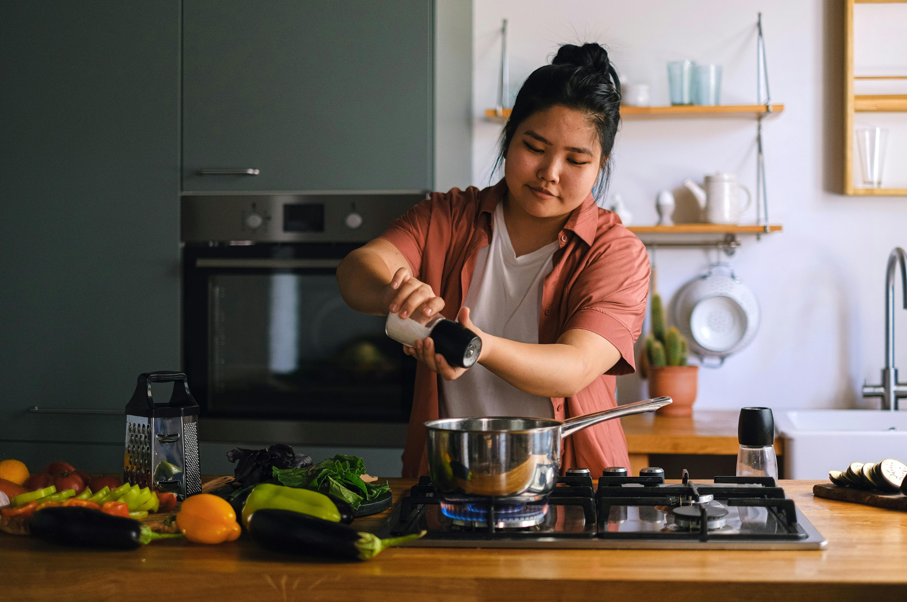 Image of Pro Chefly home chef seasoning a pot on the stove with fresh vegetables on the counter, showcasing precision and kitchen craftsmanship.