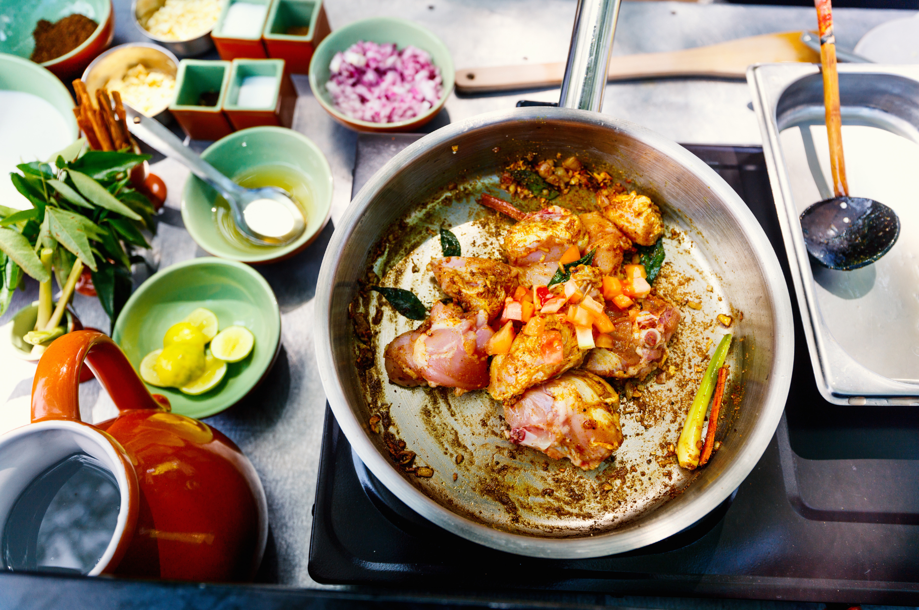 Image of Chicken simmering with spices, tomatoes, and herbs in a pan surrounded by fresh ingredients—Pro Chefly’s flavorful cooking in action.