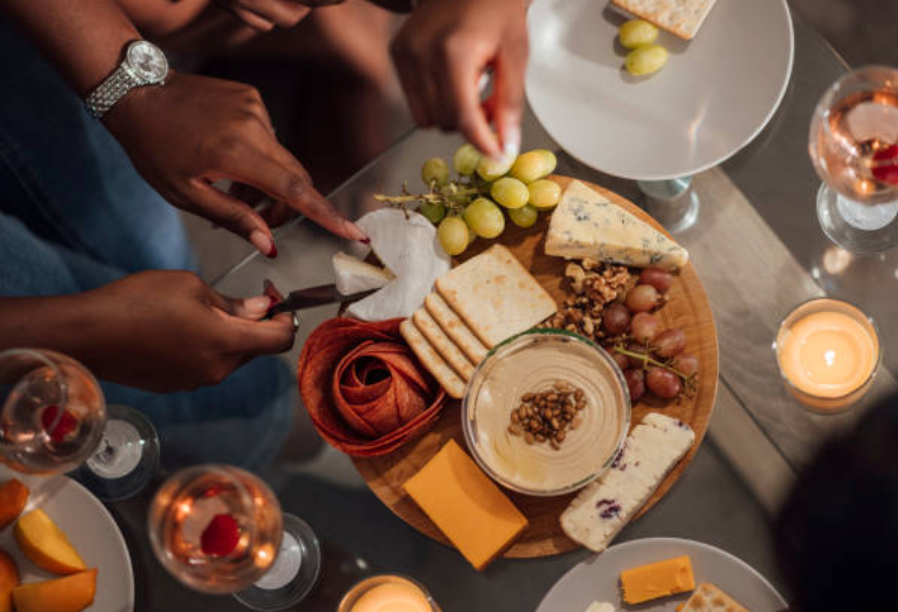 Image of Chef slicing cheese with a Pro Chefly knife on a charcuterie board with crackers, grapes, hummus, and artisan cheeses.