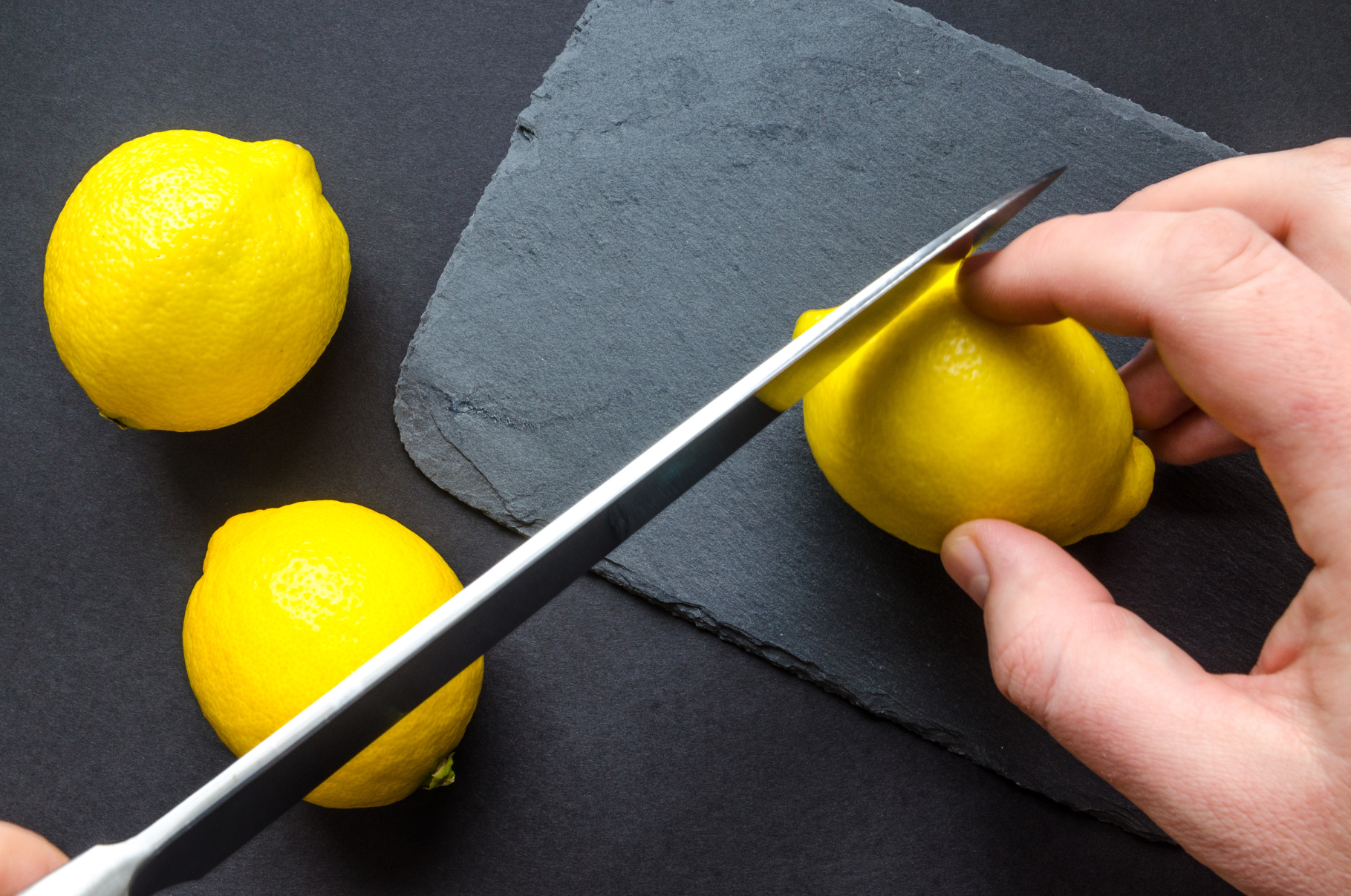 Close-up of a Damascus chef knife slicing a bright yellow lemon on a dark slate board — showcasing the razor-sharp precision and craftsmanship of Pro Chefly knives.