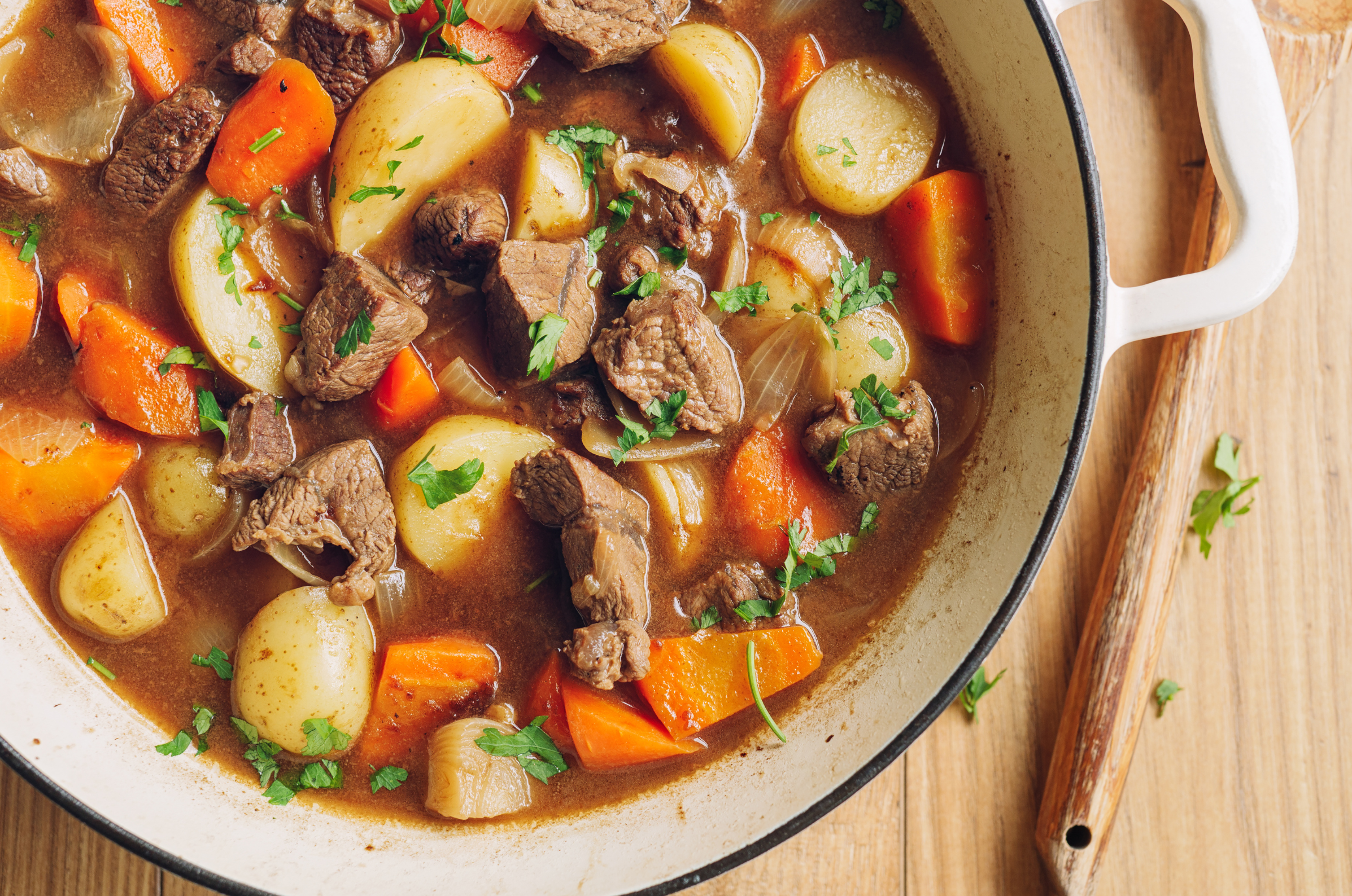 Image of Beef stew with tender beef, potatoes, and carrots in a Dutch oven, styled beside a Pro Chefly Damascus chef knife highlighting Japanese steel craftsmanship and culinary precision.
