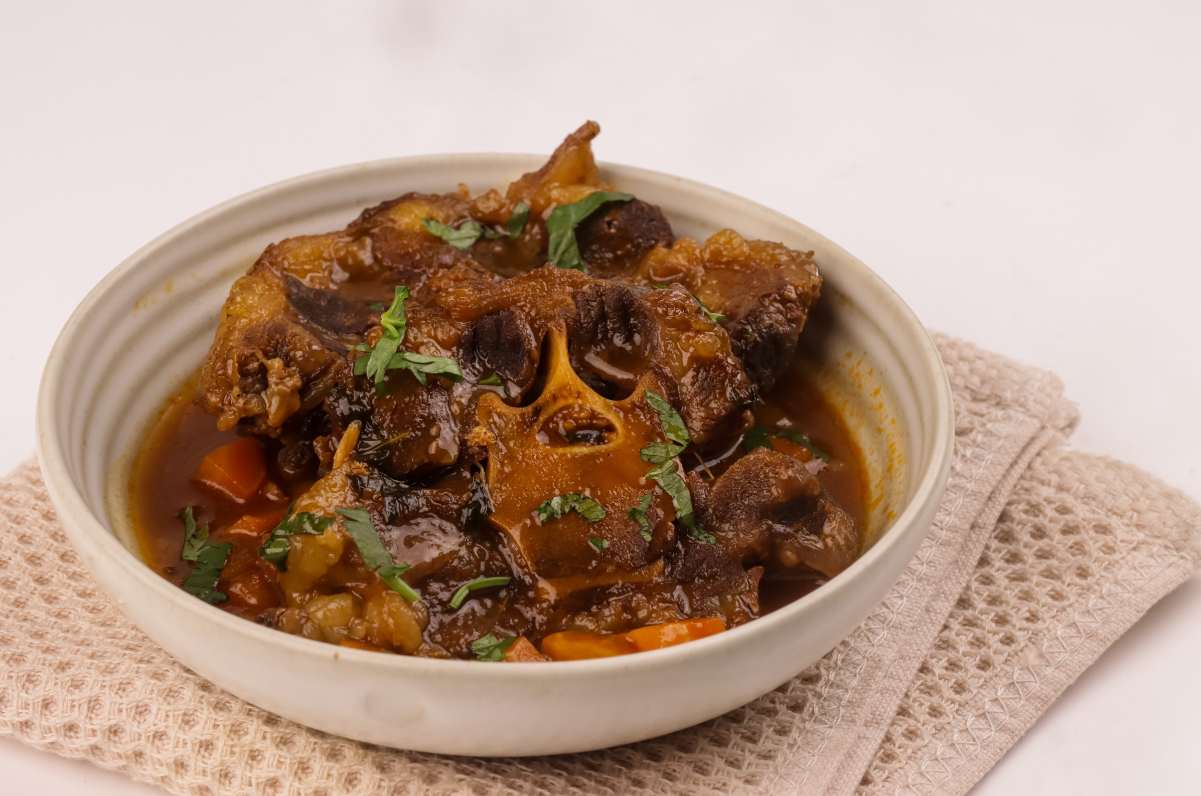 Image of Pro Chefly braised oxtails served in a rich, slow-simmered sauce with carrots, beans, and fresh herbs.