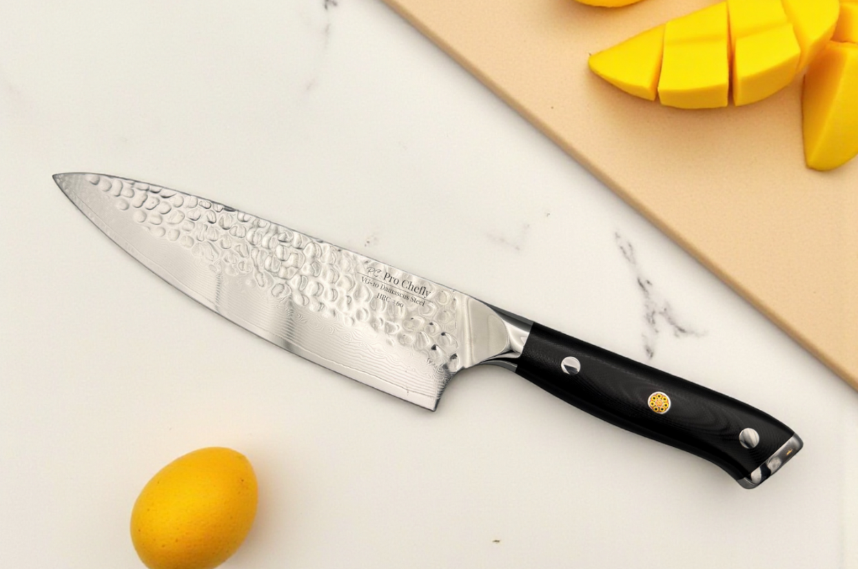 Pro Chefly VG-10 Damascus steel Japanese chef knife with a hammered finish resting on a clean marble surface beside sliced mango and lemon, showcasing premium kitchen craftsmanship.