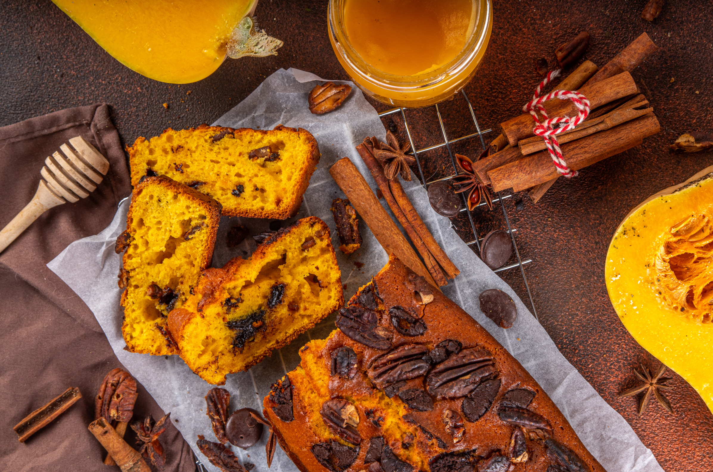 Image of Freshly sliced pumpkin bread on a wooden cutting board surrounded by mini pumpkins, pecans, and cinnamon sticks, perfectly cut with a Pro Chefly Damascus bread knife.