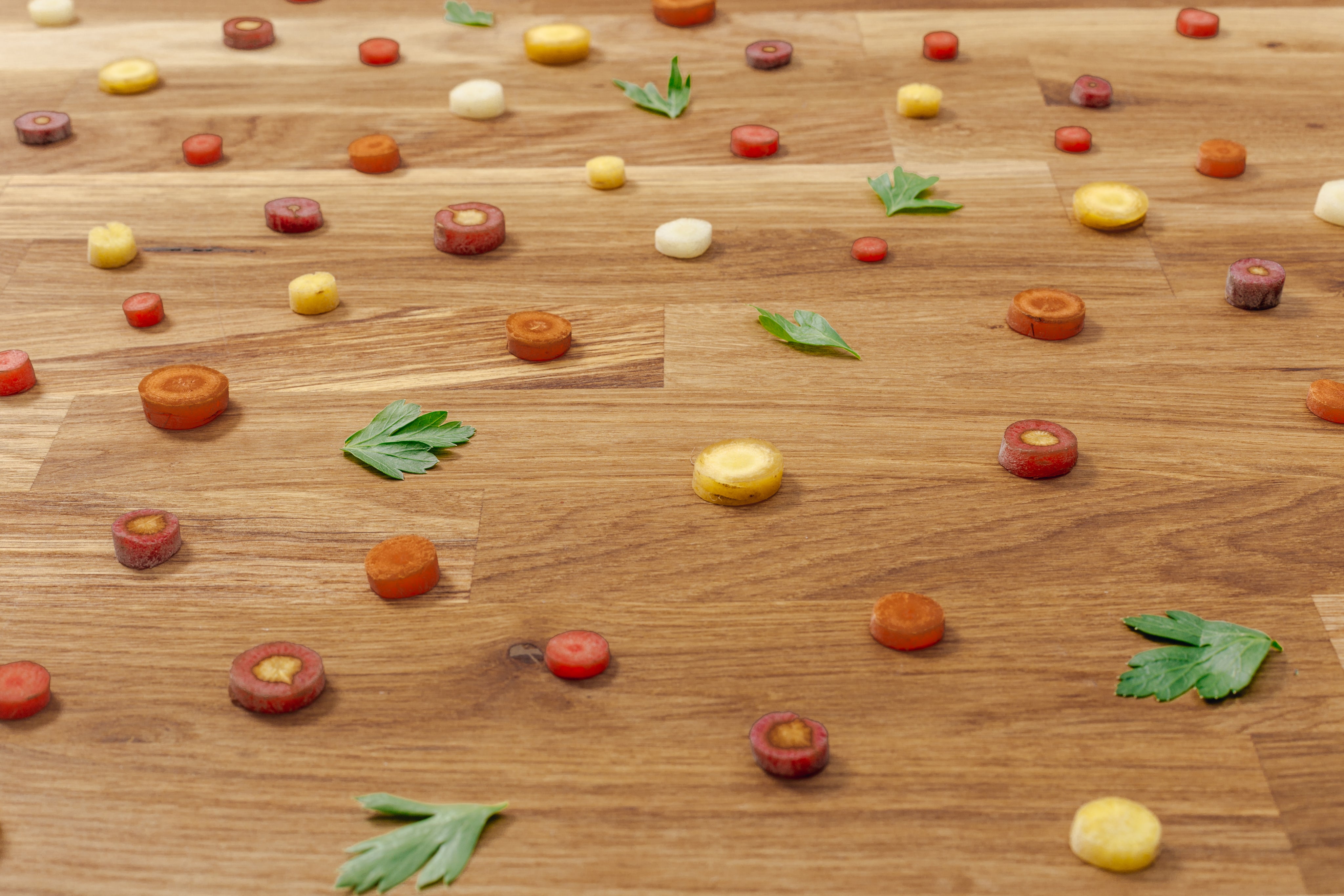 Colorful carrot slices and parsley leaves scattered on a wooden surface — perfect prep work with a Pro Chefly petty knife.