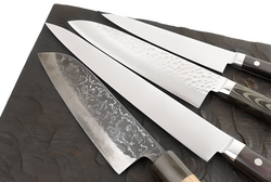 Image of Set of Japanese Damascus chef knives with patterned steel blades and wooden handles, displayed on a dark textured cutting board – Pro Chefly