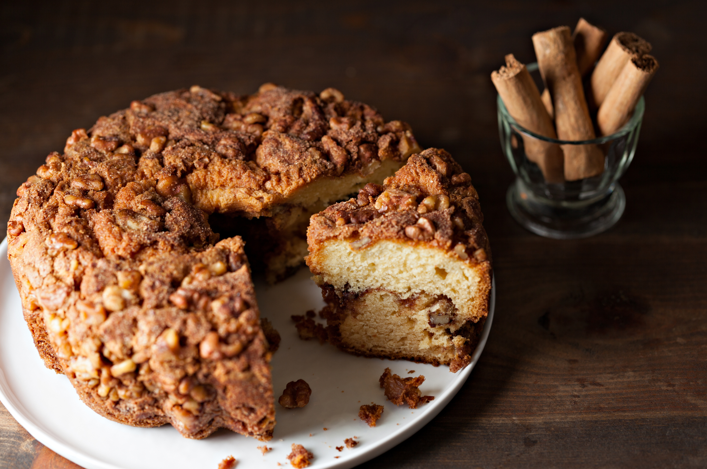 Image of Pro Chefly cozy winter cinnamon coffee cake with pecan crumble topping served on a white plate beside whole cinnamon sticks for seasonal baking inspiration