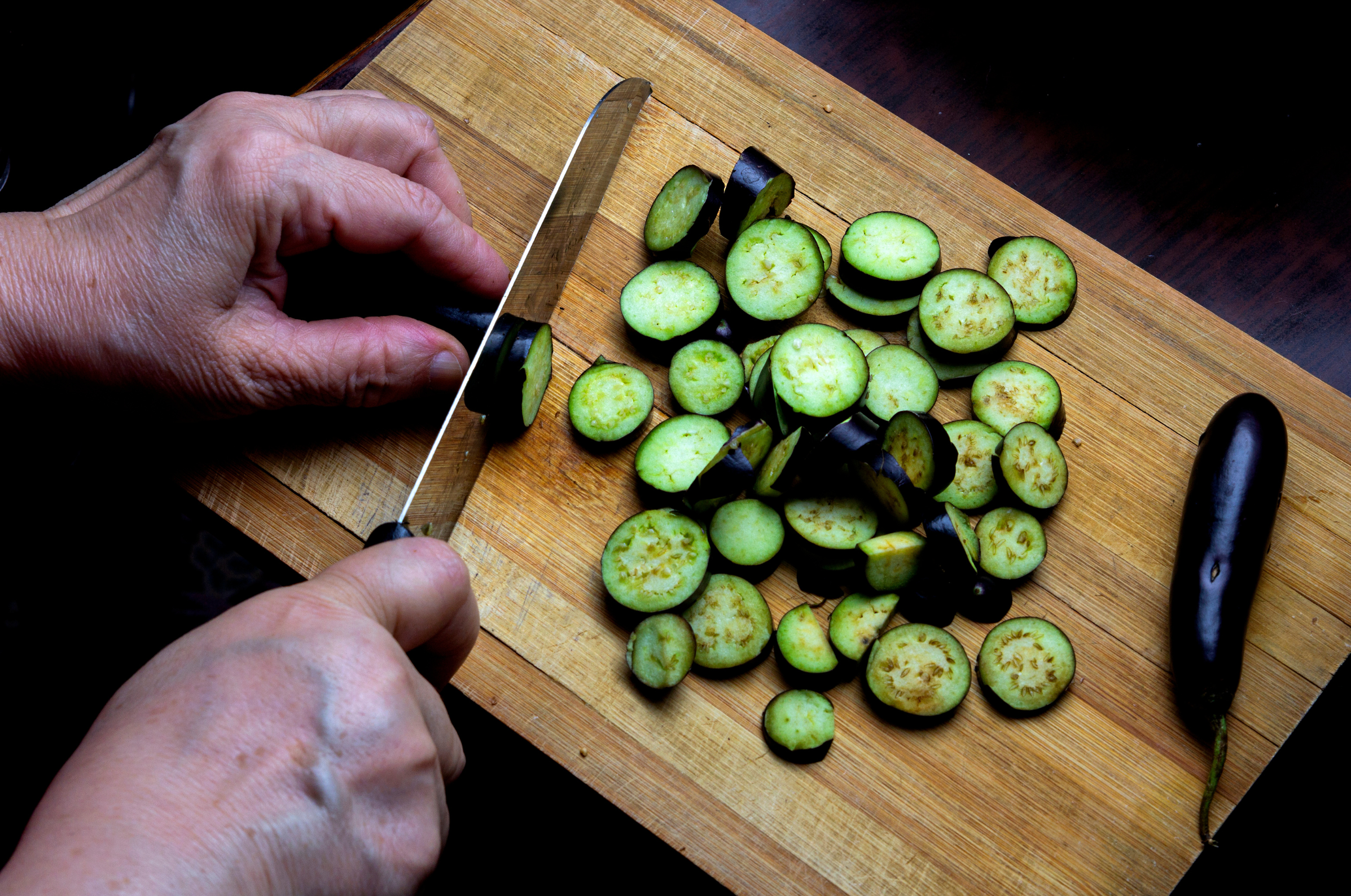 pro chefly japanese knife slicing fresh eggplant rounds on a wooden cutting board for meal prep