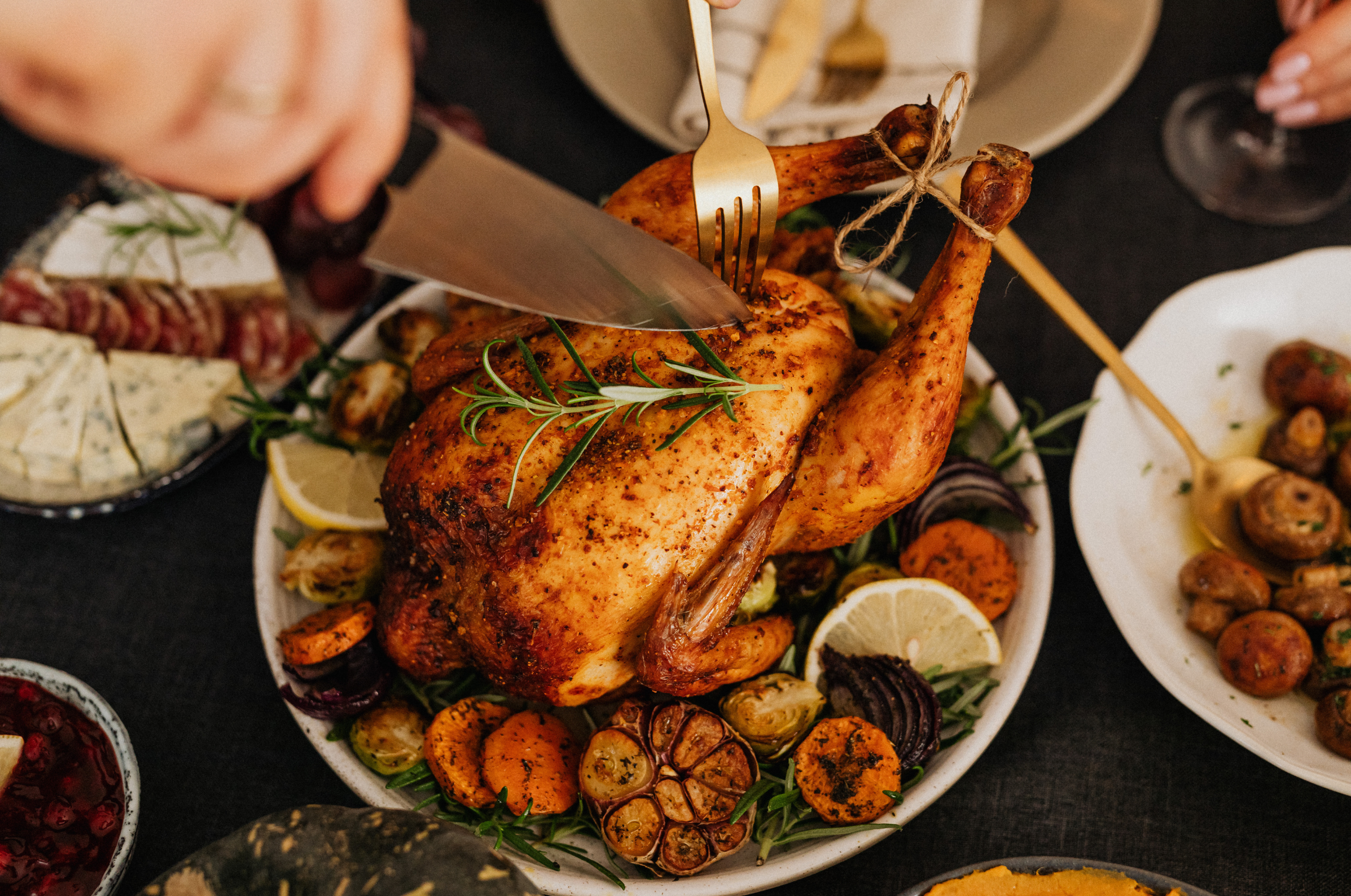 pro chefly japanese knife carving roasted whole chicken surrounded by vegetables on a holiday dinner table