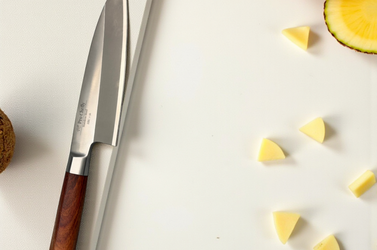 Pro Chefly Japanese knife on a white cutting board beside sliced pineapple pieces, showcasing the sleek blade and wood handle.