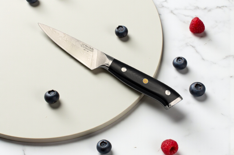 Pro Chefly Damascus paring knife on a round board with scattered blueberries and raspberries.