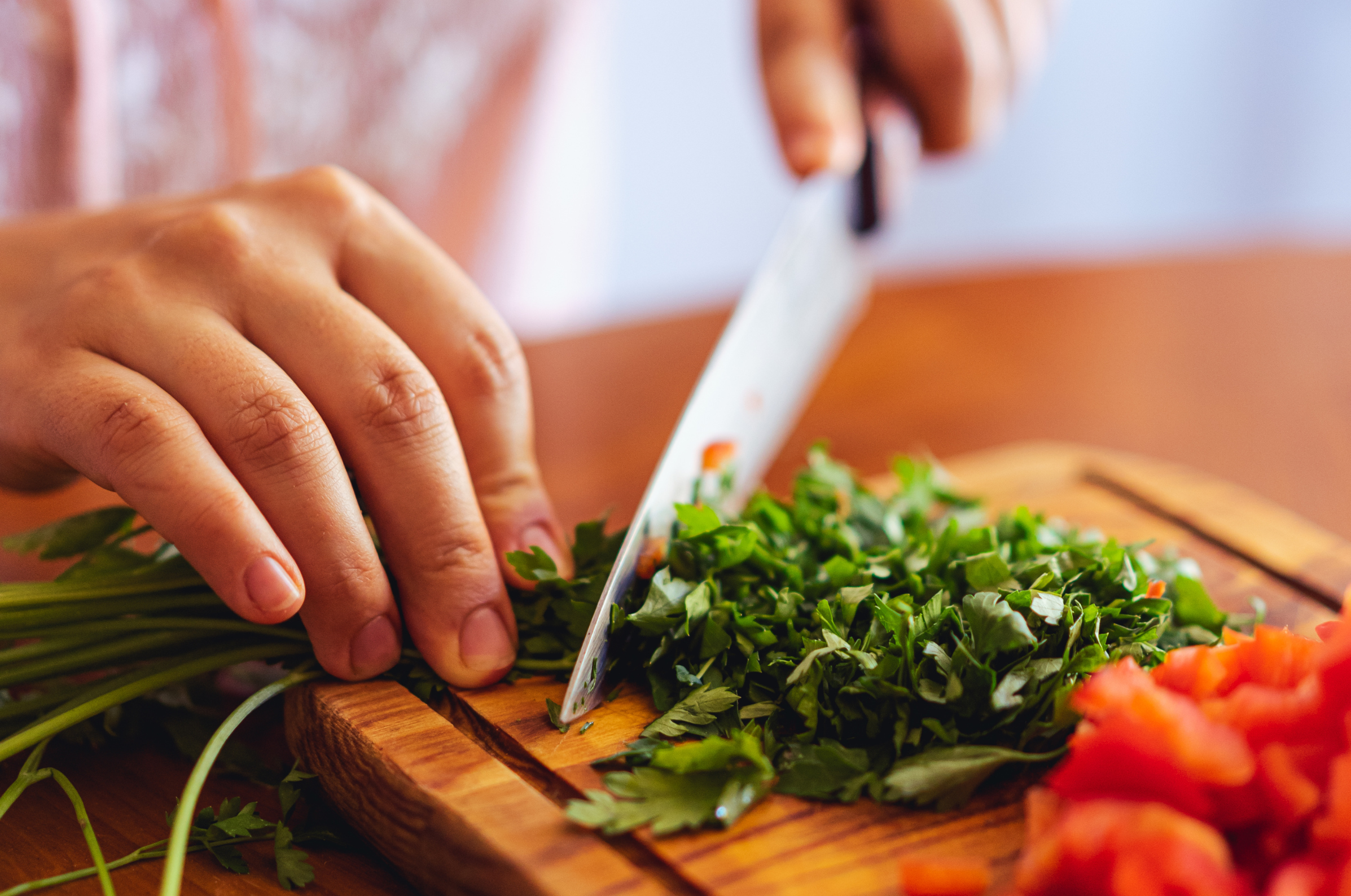 Image of Hands chopping fresh herbs with a sharp Japanese knife on a wooden board.