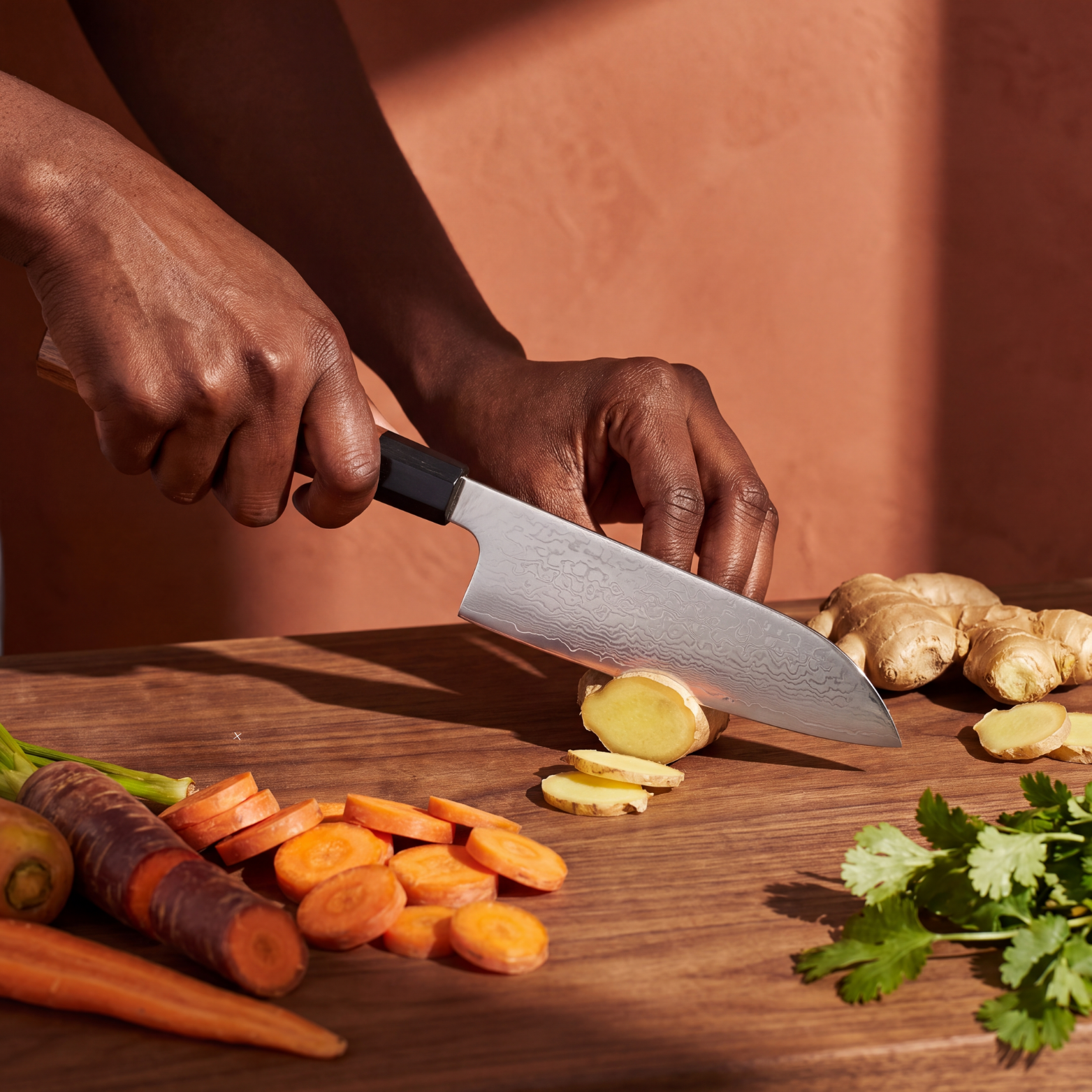 Image of Pro Chefly 7-inch Damascus santoku knife with rosewood wa handle, slicing fresh ginger on a walnut board with rainbow carrots