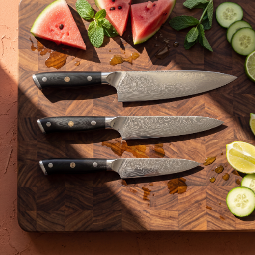 Image of Pro Chefly 3-piece Damascus knife set with black riveted handles, overhead on an end-grain board with watermelon, cucumber and lime