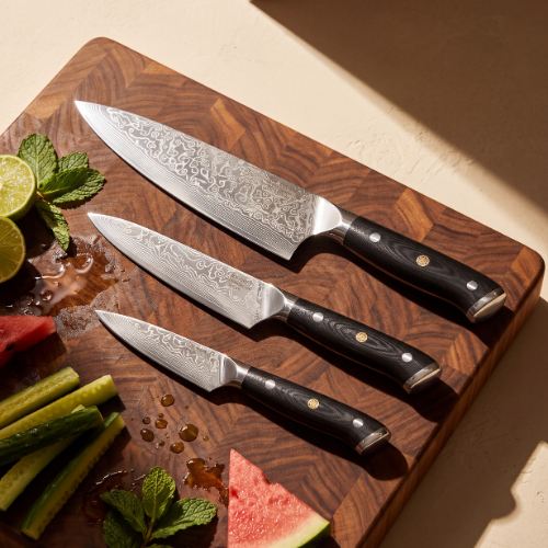 Image of Pro Chefly 3-piece Damascus knife set with black riveted handles, fanned on a walnut board with lime, cucumber and mint