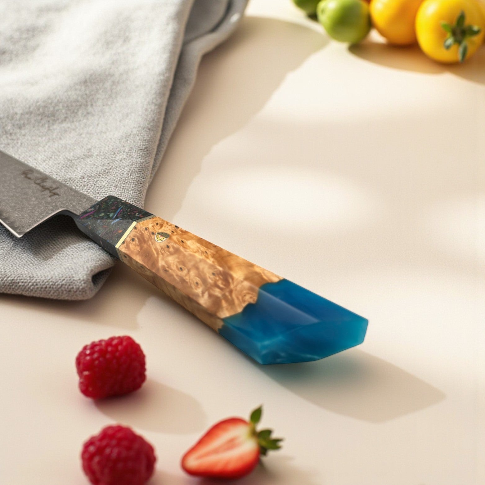 Image of Pro Chefly AUS-10 Damascus steel Japanese gyuto knife with resin and wood handle resting on marble beside berries and a kitchen towel.