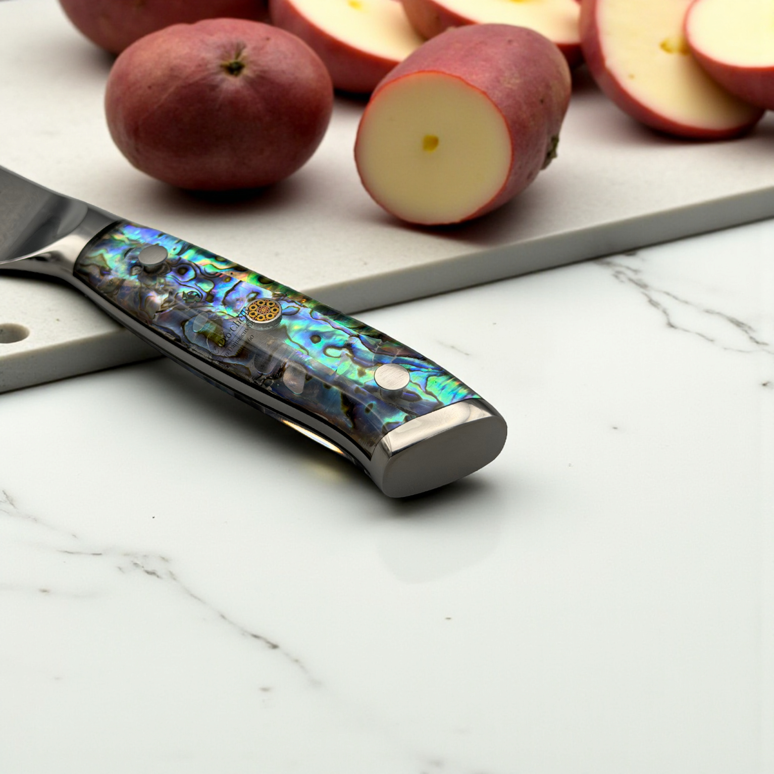 Image of Pro Chefly VG-10 Damascus Santoku Knife with resin handle next to halved red potatoes on a marble surface.